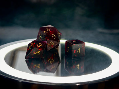 Czarne kostki RPG z czerwonymi drobinkami i złotymi cyframi na lustrzanej tacy