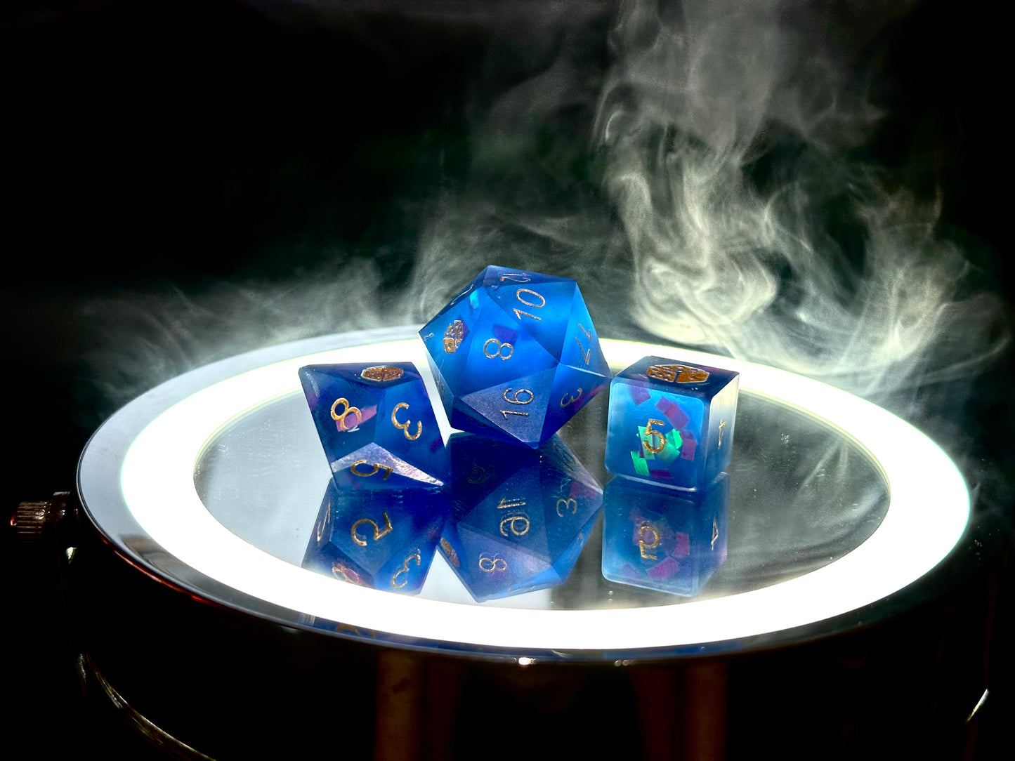 Niebieskie kostki RPG z żywicy z holo efektem, d20, d8, d6 na lustrze, otoczone dymem