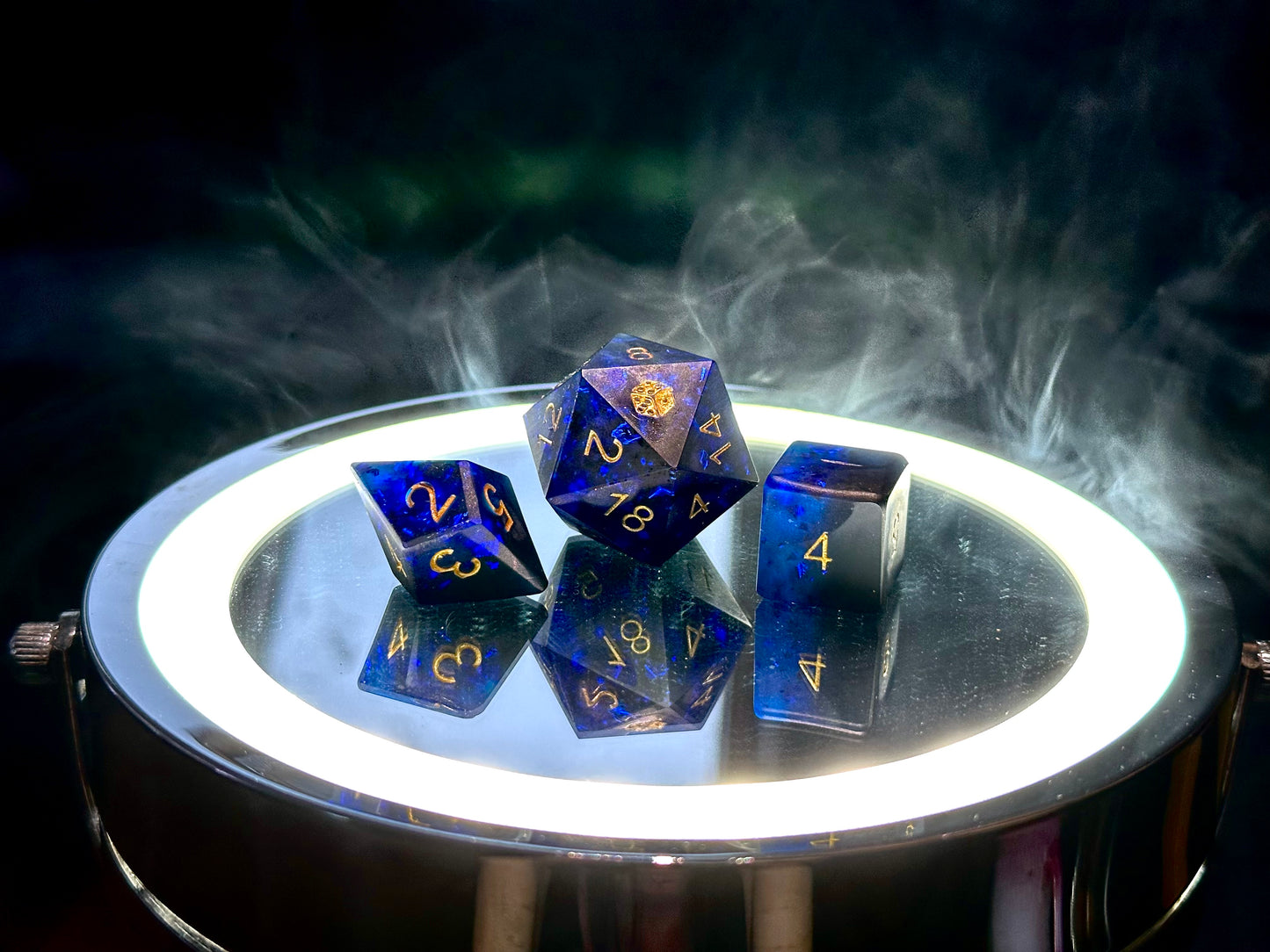 Niebiesko-czarne żywiczne kostki RPG d20, d8 i d6 z złotymi cyframi na lustrzanej tacy.