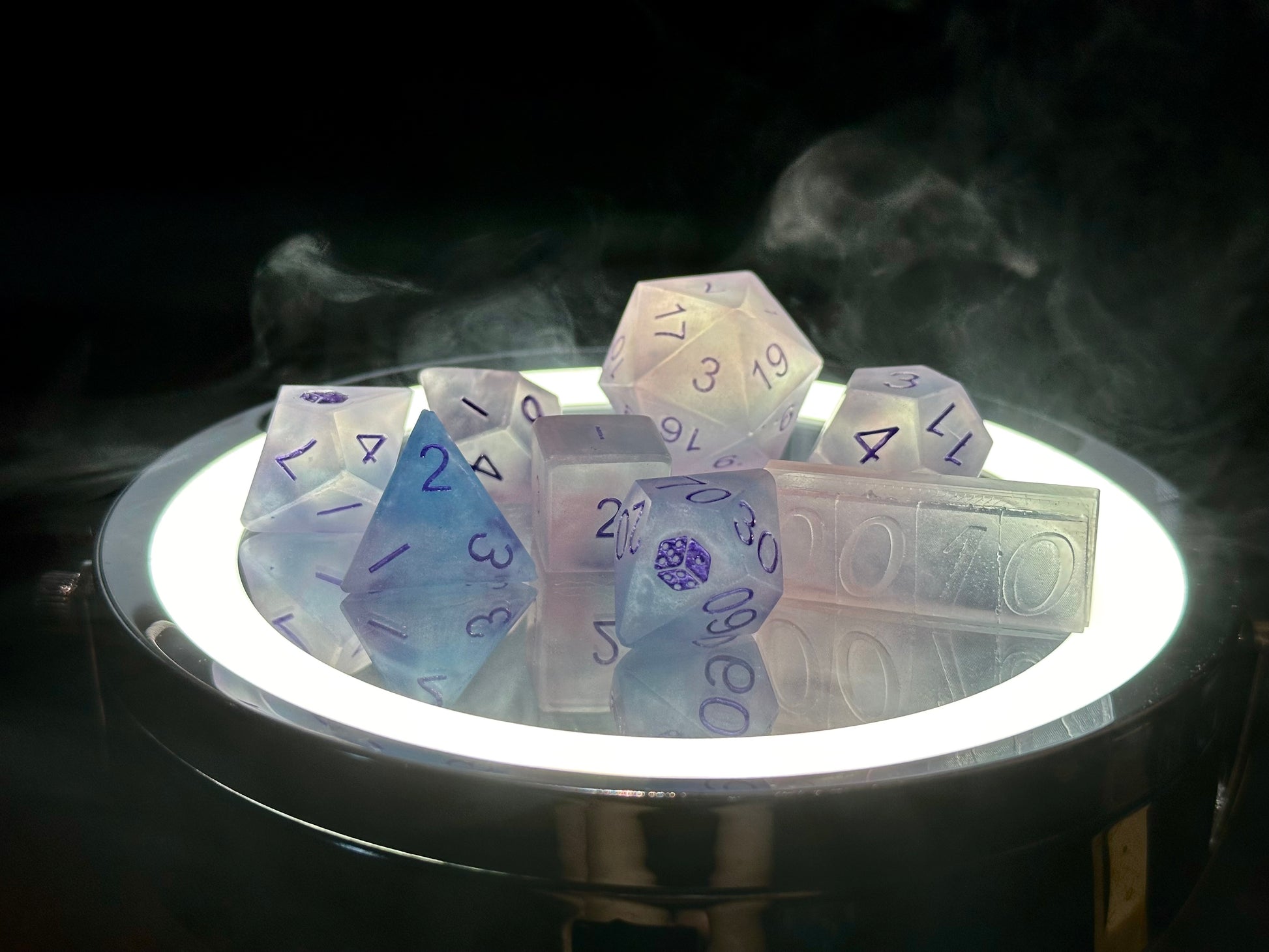 Pudrowo różowy zestaw ręcznie robionych kostek RPG z żywicy na podświetlonym tle